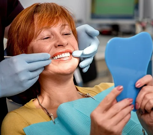 woman in exam chair looking at dentures after fitting - Dentaluxe